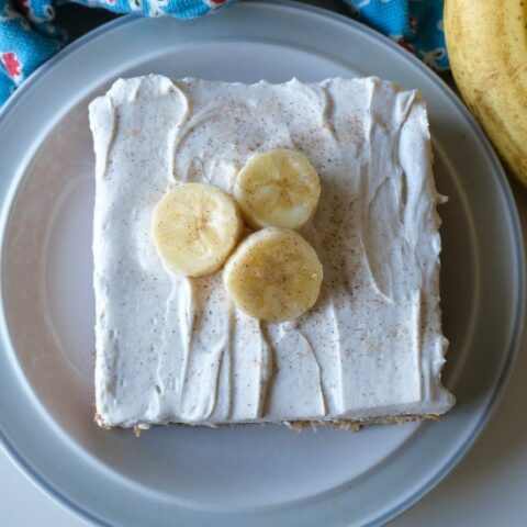 square cake with white frosting and three banana slices on a blue and white plate