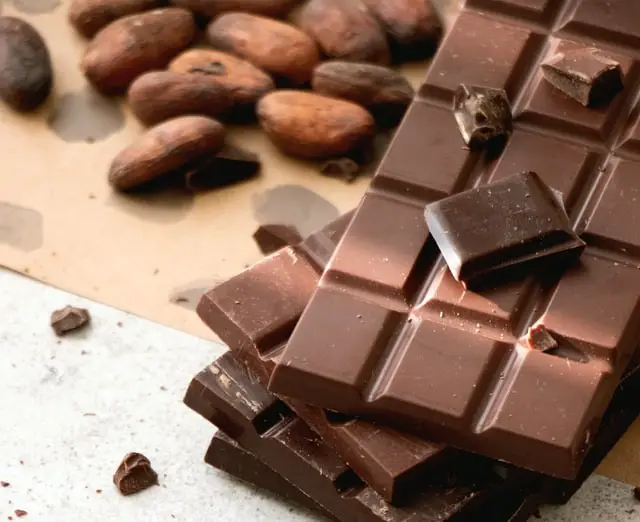 Two milk chocolate bars rest on two dark chocolate bars. Several cocoa beans are in the background.