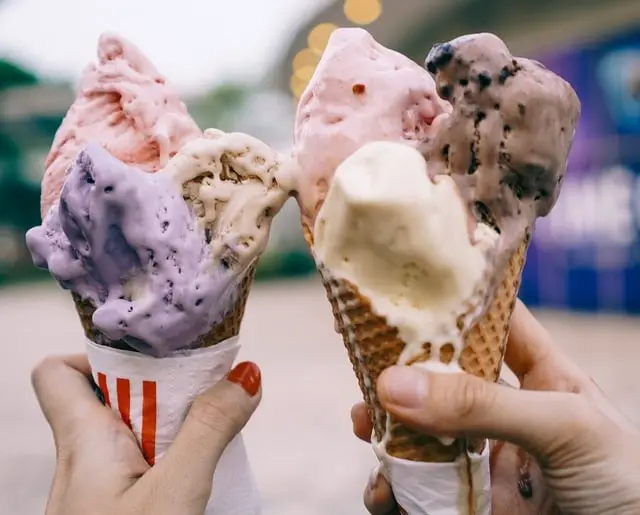 two ice cream cones being held side by side with melting ice cream