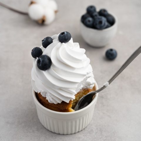 white ramekin of cake with large swirl of whipped cream topped with blueberries