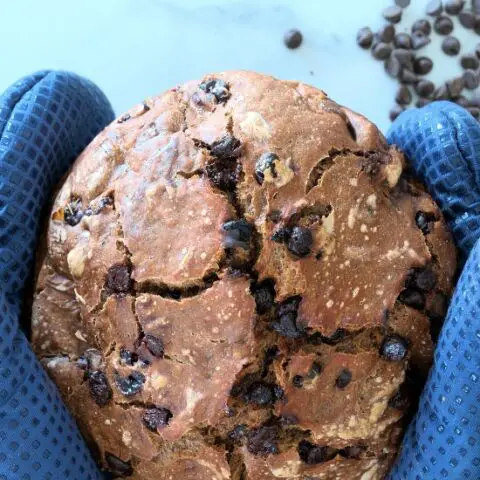 loaf of artisan bread held by two hands in blue oven mitts