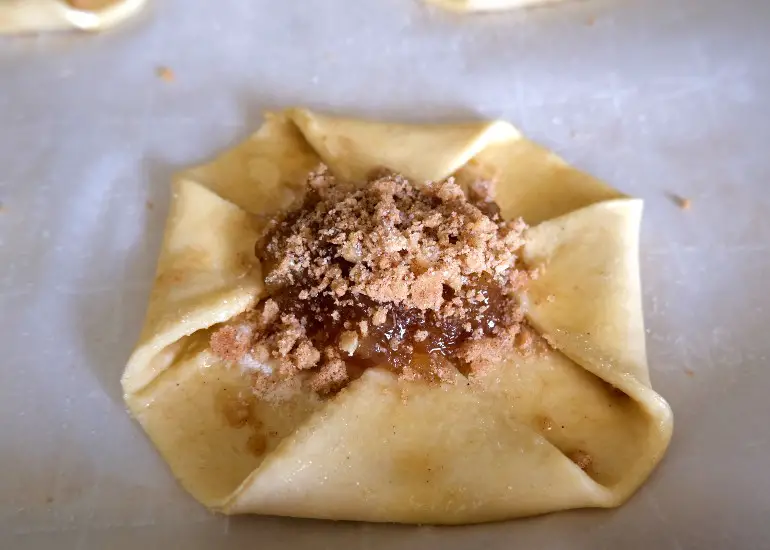 raw danish with edges folded in and apple pie filling in the center