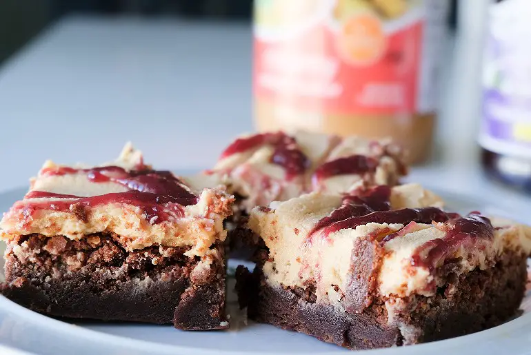 3 brownies arranged on a blue plate with peanut butter and jelly in the background