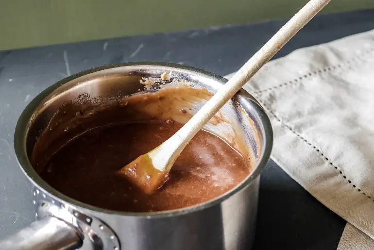 image of chocolate pudding being stirred in a saucepan with a wooden spoon