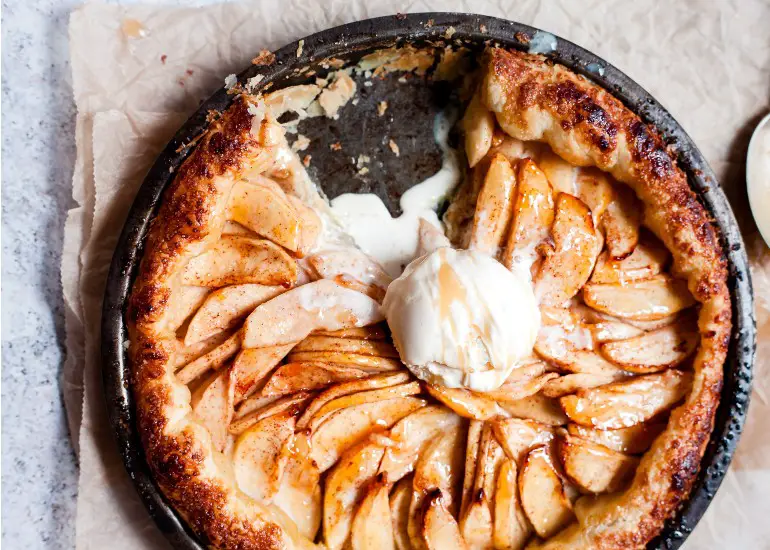 apple tart in a black pan with a melting scoop of ice cream on top