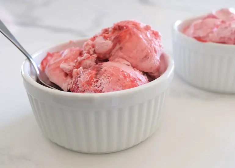 3 scoops of strawberry ice cream in a white bowl with a spoon
