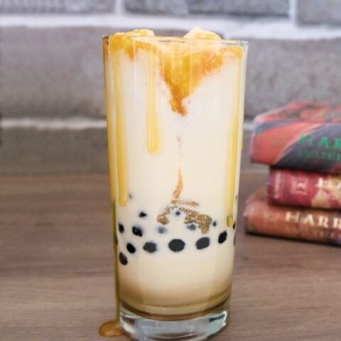 tall glass containing a milkshake with boba in the bottom, harry potter books are stacked up in the background