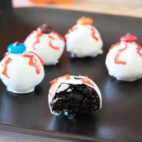 5 eyeball truffles arranged on a black plate, one with a bite taken out