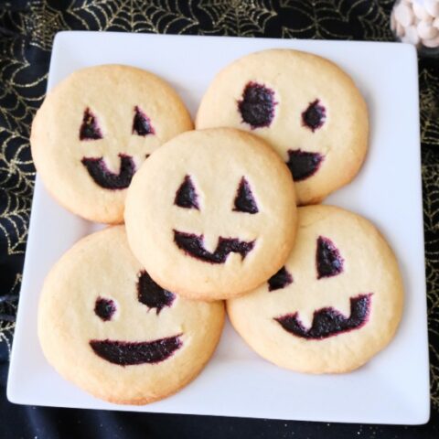 5 jack-o-lantern cookies on a white cake with a black background