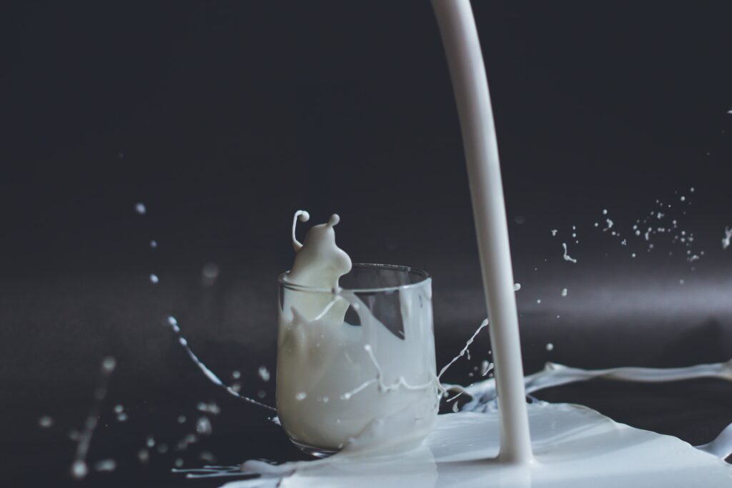 milk is being poured onto a black surface with a glass of milk behind it