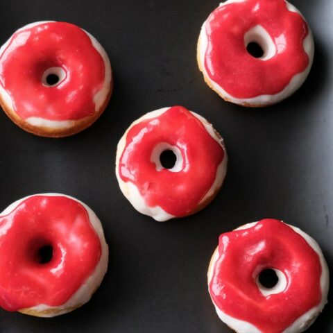 5 donuts with white and red icing arranged on a black plate