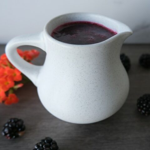 blackberry syrup in a white dish with blackberries and orange flowers around