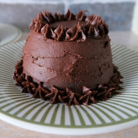 small brown cake with frosting on the outside on a green striped plate