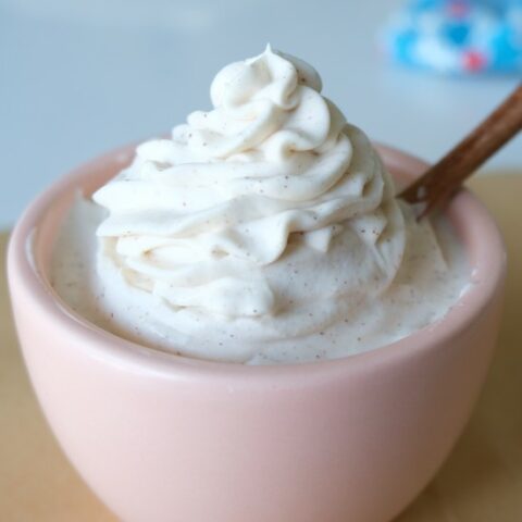 swirl of white frosting in small pink bowl with a tiny wooden spoon in it