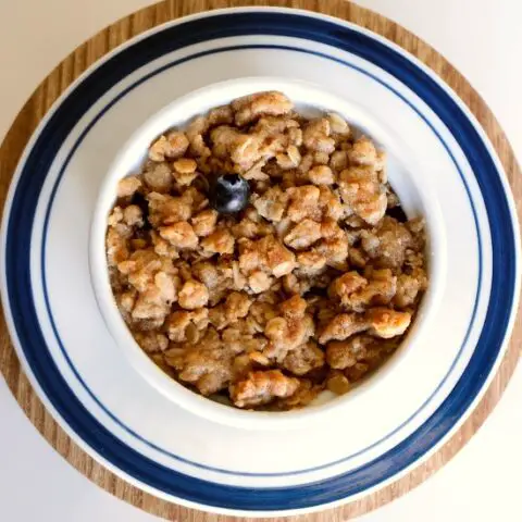 brown crisp in a white dish with a blueberry on top. The dish is on a white and blue plate.