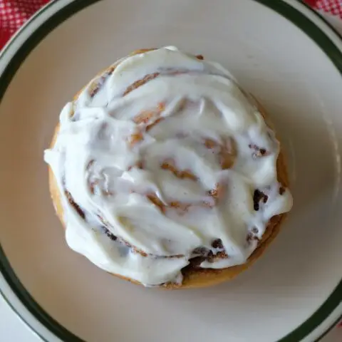 overhead shot of a cinnamon roll spread with white frosting sitting on a white plate with green around the edge