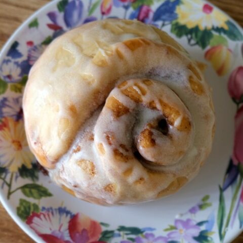 cinnamon roll drizzled with glaze on a floral plate